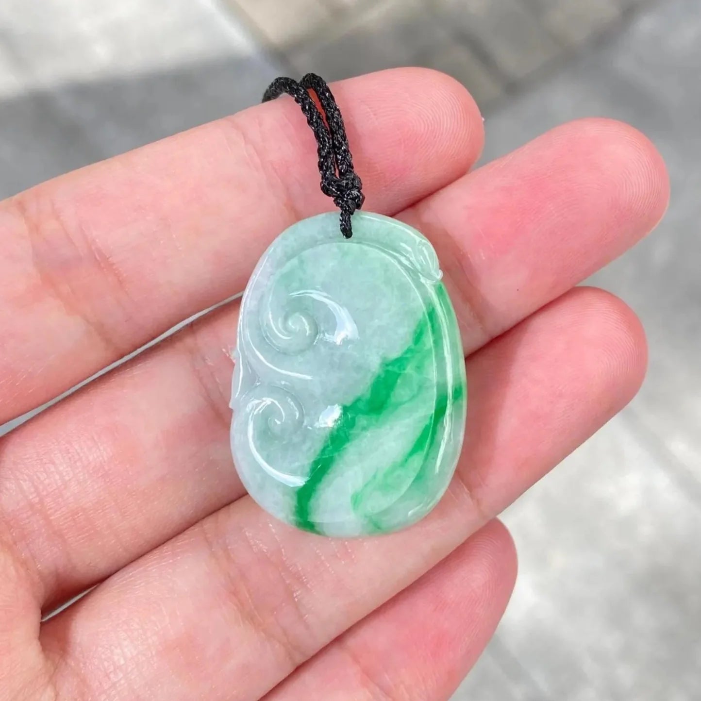 Green jade pendant held in a hand with a blurred background